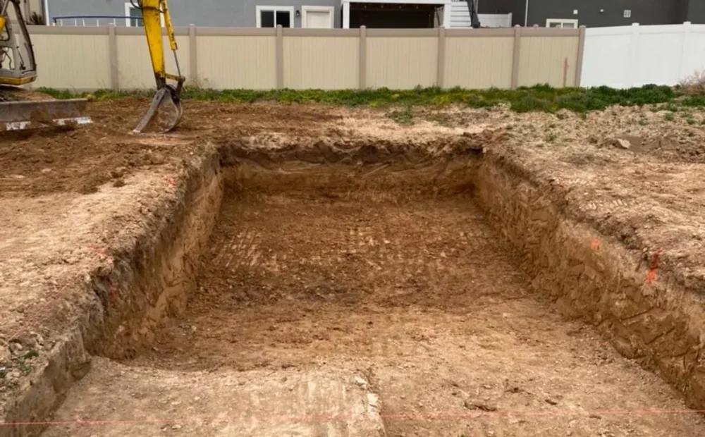 Custom swimming pool excavation underway with excavator in a residential backyard in Salem, Utah.
