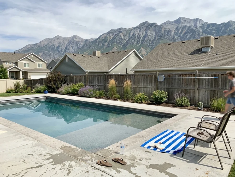 Completed custom gunite pool with tanning ledge and concrete decking in a Lehi backyard